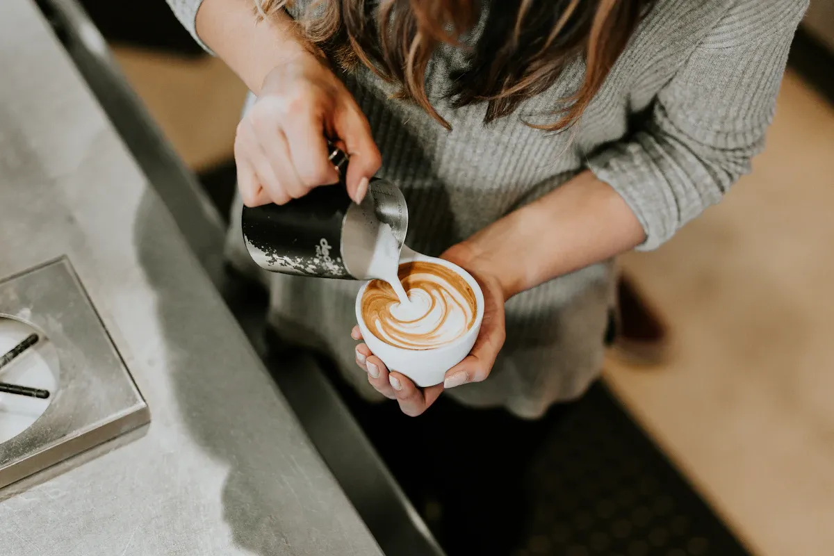 A barista pouring milk at the bar